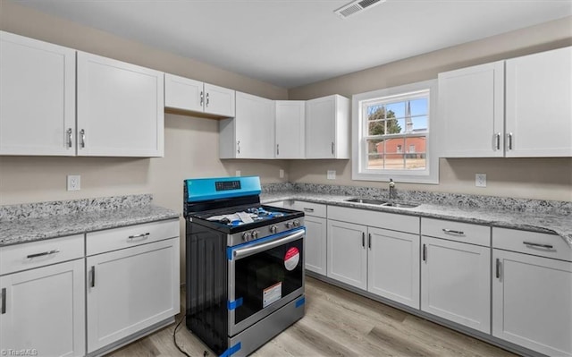 kitchen featuring a sink, white cabinets, light wood-type flooring, and stainless steel gas range oven