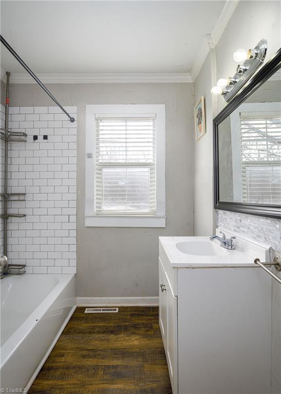 bathroom featuring baseboards, wood finished floors,  shower combination, crown molding, and vanity