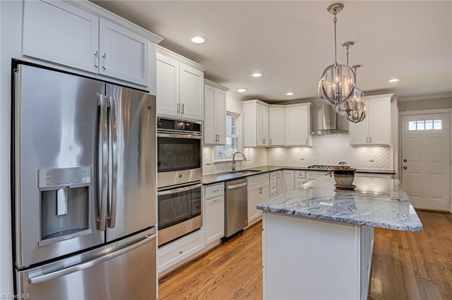 kitchen featuring white cabinetry, sink, a center island, stainless steel appliances, and wall chimney range hood