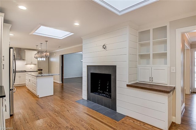 kitchen with white cabinetry, hanging light fixtures, a skylight, a fireplace, and a kitchen island