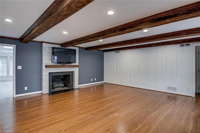 unfurnished living room with light wood-type flooring, a large fireplace, and beam ceiling