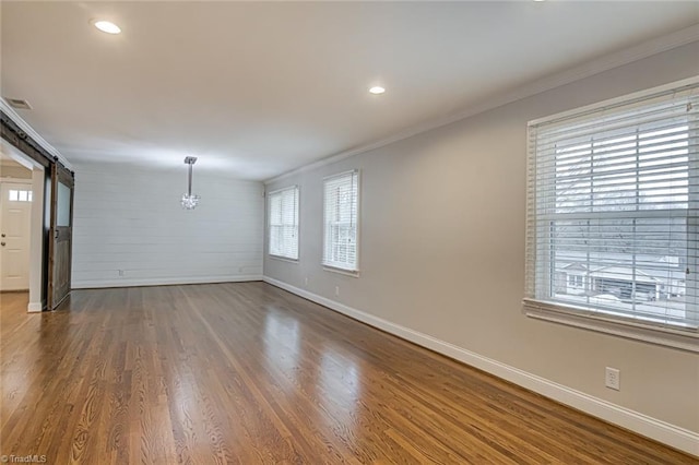 unfurnished living room with crown molding, a barn door, and dark hardwood / wood-style floors