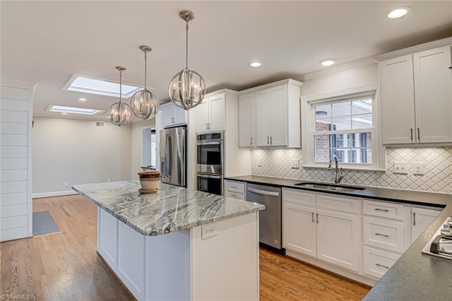 kitchen featuring sink, appliances with stainless steel finishes, white cabinets, a kitchen island, and decorative light fixtures