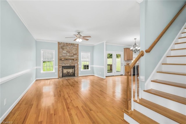 unfurnished living room with light wood-type flooring, ceiling fan with notable chandelier, a fireplace, and crown molding