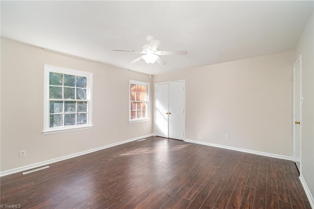 empty room featuring dark wood-style floors, baseboards, visible vents, and a ceiling fan