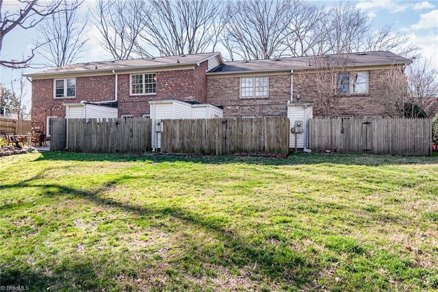 rear view of property featuring brick siding, a lawn, and fence