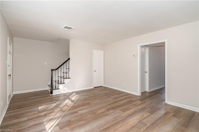 unfurnished room with stairway, wood finished floors, visible vents, and baseboards