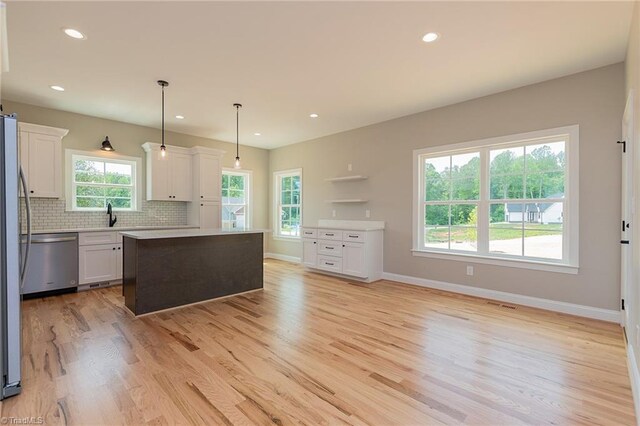 kitchen with decorative backsplash, appliances with stainless steel finishes, a center island, white cabinets, and light wood-style floors