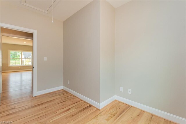 unfurnished room featuring light wood-type flooring, attic access, and baseboards