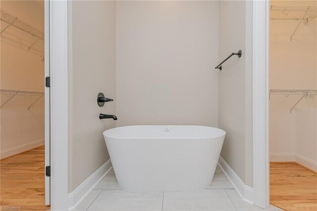 full bathroom featuring a walk in closet, a freestanding tub, and baseboards