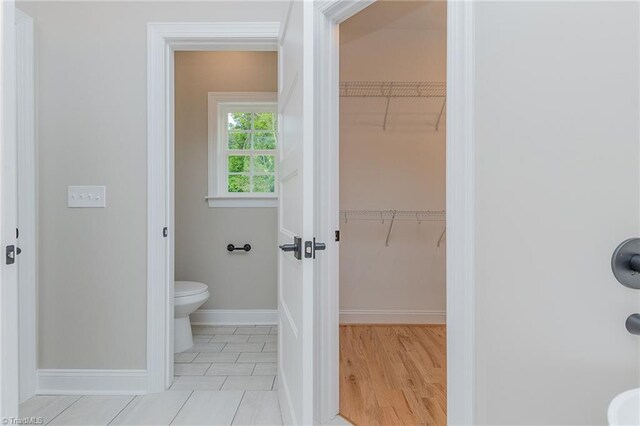 bathroom featuring baseboards, wood finished floors, a spacious closet, and toilet
