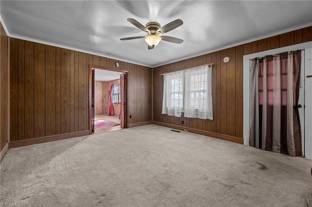 carpeted spare room with crown molding, wooden walls, and ceiling fan