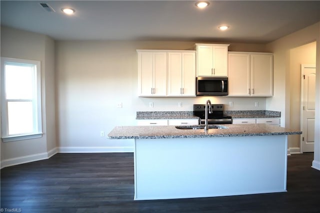 kitchen with appliances with stainless steel finishes, white cabinetry, sink, light stone counters, and a center island with sink