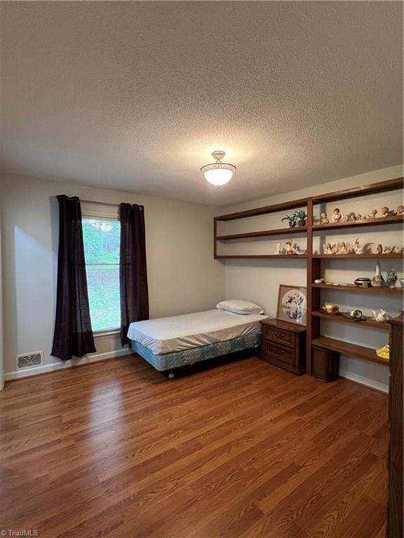 bedroom with visible vents, baseboards, a textured ceiling, and wood finished floors