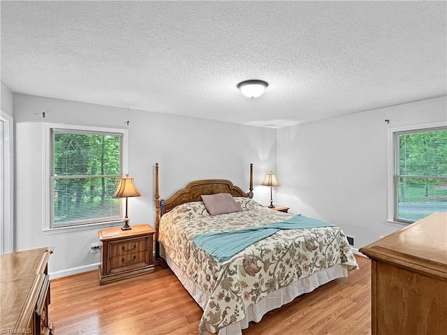 bedroom featuring a textured ceiling, multiple windows, and light wood finished floors