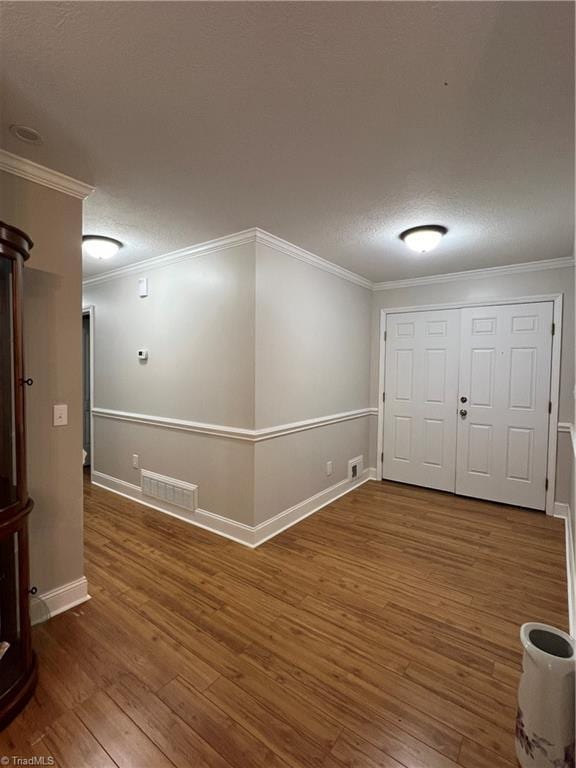 unfurnished room with crown molding, visible vents, baseboards, a textured ceiling, and hardwood / wood-style flooring
