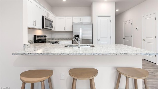 kitchen with kitchen peninsula, light stone countertops, a breakfast bar, stainless steel appliances, and white cabinets