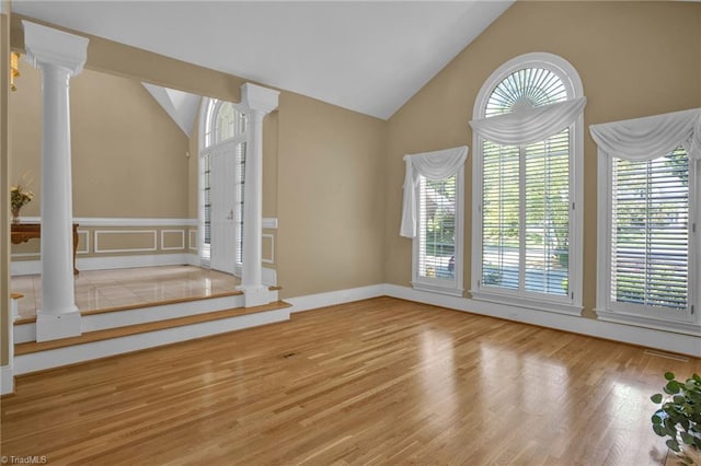 unfurnished living room featuring high vaulted ceiling, light hardwood / wood-style flooring, and ornate columns