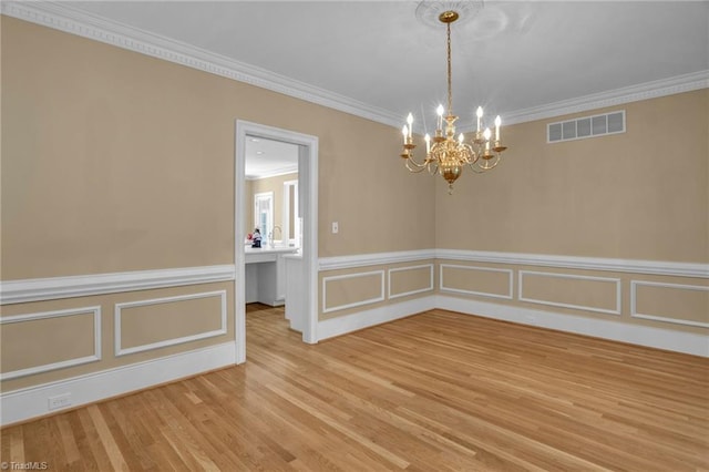 spare room featuring wood-type flooring, crown molding, and a notable chandelier