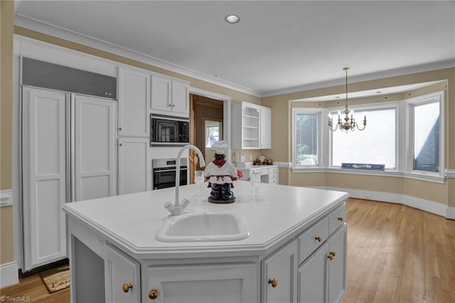 kitchen with built in appliances, a center island with sink, and light hardwood / wood-style floors