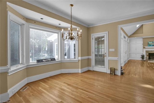 unfurnished dining area featuring lofted ceiling, a chandelier, hardwood / wood-style flooring, and a stone fireplace