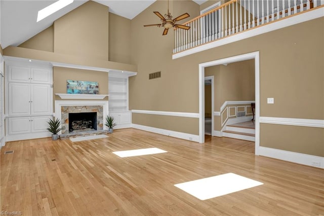 unfurnished living room with light hardwood / wood-style floors, a stone fireplace, ceiling fan, and high vaulted ceiling