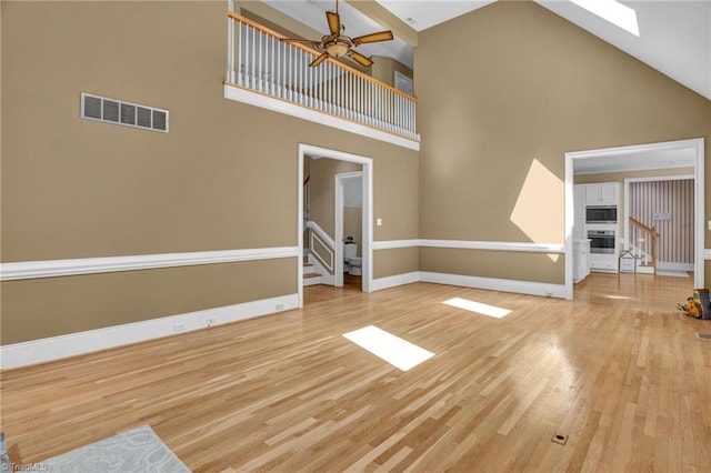 unfurnished living room featuring light hardwood / wood-style flooring, ceiling fan, a skylight, and high vaulted ceiling