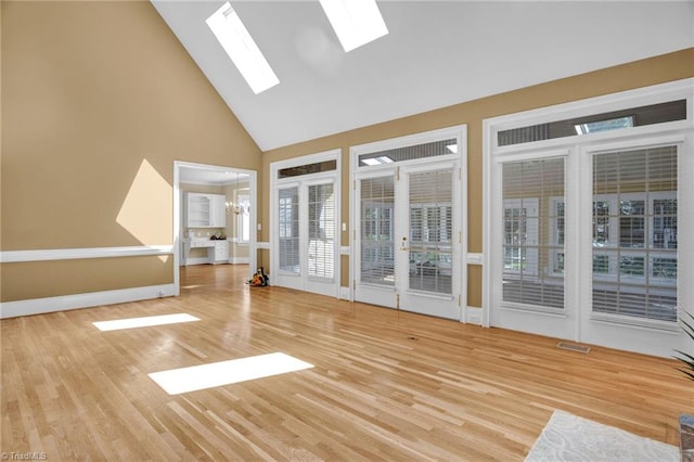 unfurnished living room featuring high vaulted ceiling, light hardwood / wood-style floors, a skylight, and a healthy amount of sunlight