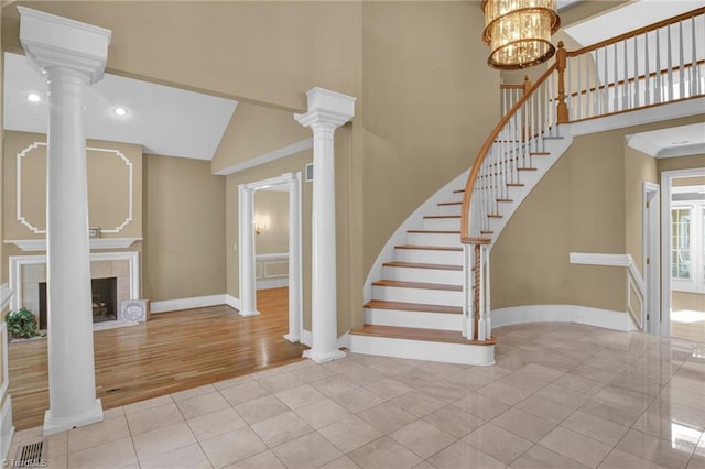 stairway with wood-type flooring, a chandelier, a fireplace, and ornate columns