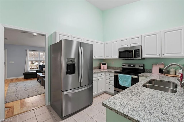 kitchen with stainless steel appliances, sink, white cabinetry, light tile patterned floors, and light stone countertops