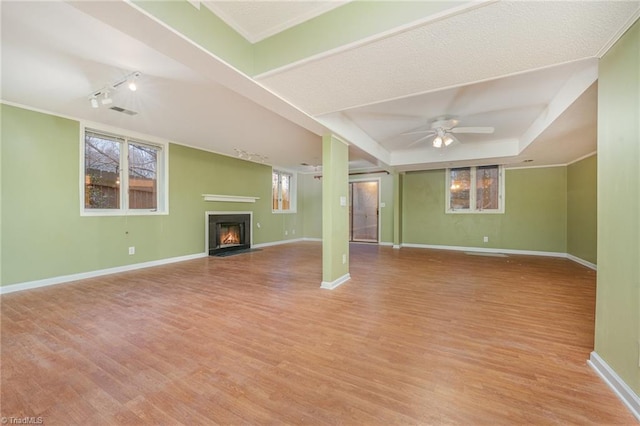 unfurnished living room featuring crown molding, ceiling fan, a raised ceiling, and light wood-type flooring