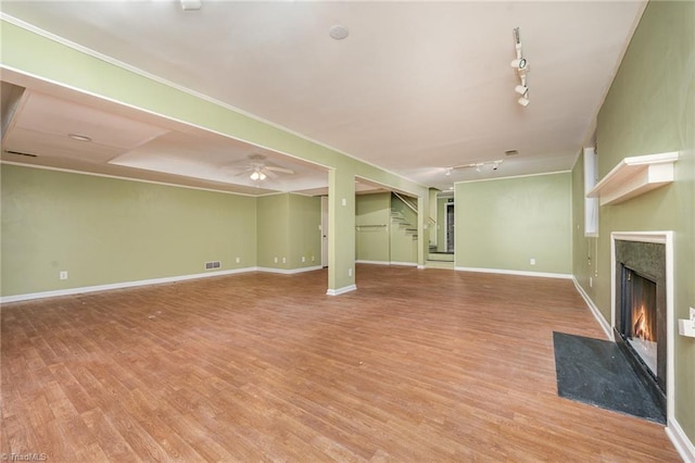 unfurnished living room with ceiling fan, a high end fireplace, rail lighting, and light wood-type flooring