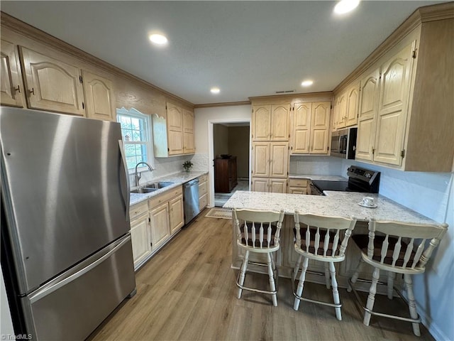 kitchen with light brown cabinets, appliances with stainless steel finishes, a peninsula, light wood-style floors, and a sink