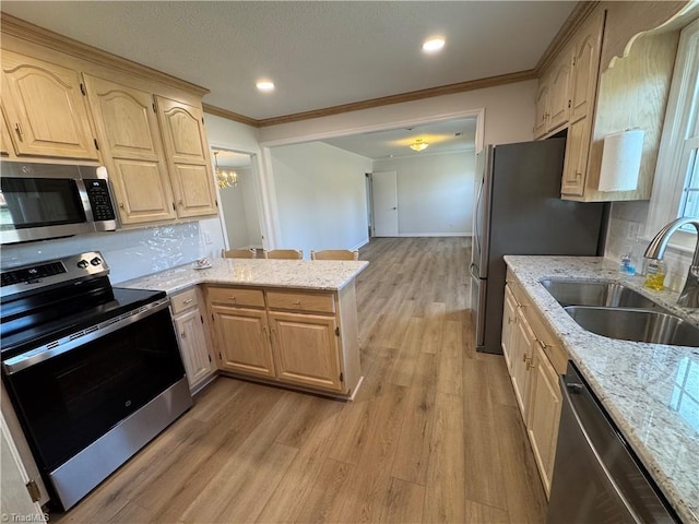 kitchen with a peninsula, a sink, light wood-style floors, appliances with stainless steel finishes, and crown molding