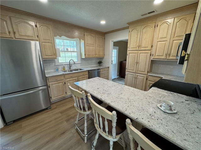 kitchen with light brown cabinets, light stone countertops, a breakfast bar, a sink, and stainless steel appliances