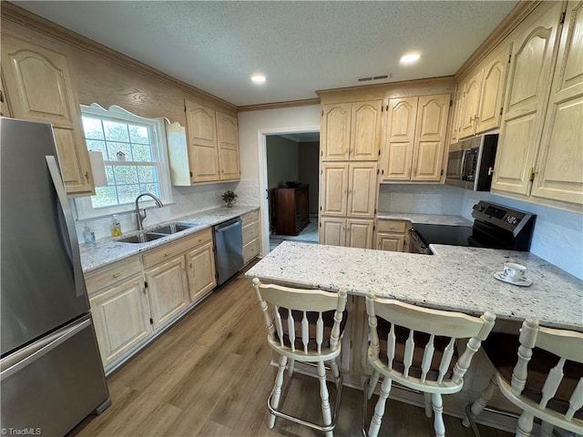 kitchen featuring visible vents, light brown cabinetry, a sink, stainless steel appliances, and light wood-style floors