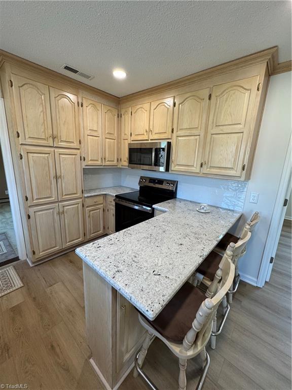 kitchen with stainless steel microwave, light brown cabinets, electric range oven, and wood finished floors