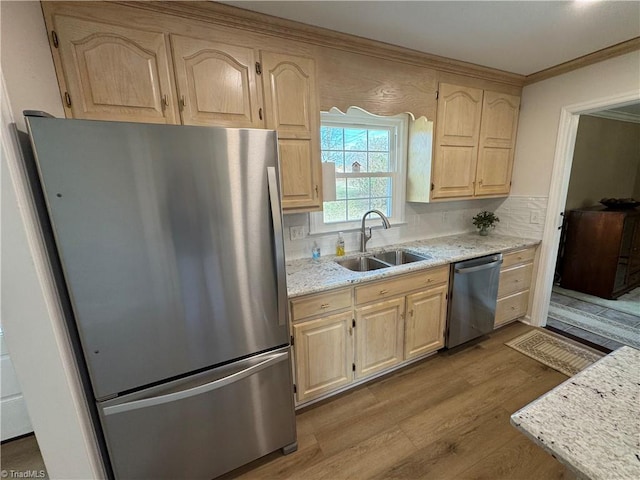 kitchen with light brown cabinetry, ornamental molding, a sink, appliances with stainless steel finishes, and light wood-type flooring