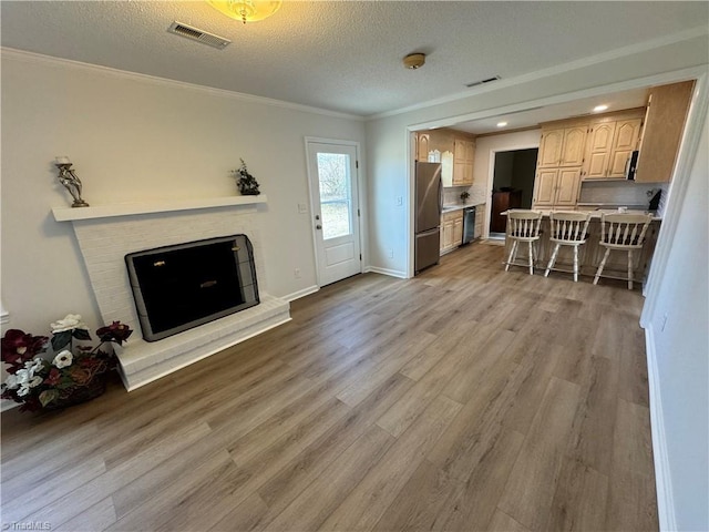 living area with light wood-type flooring, visible vents, a brick fireplace, and ornamental molding