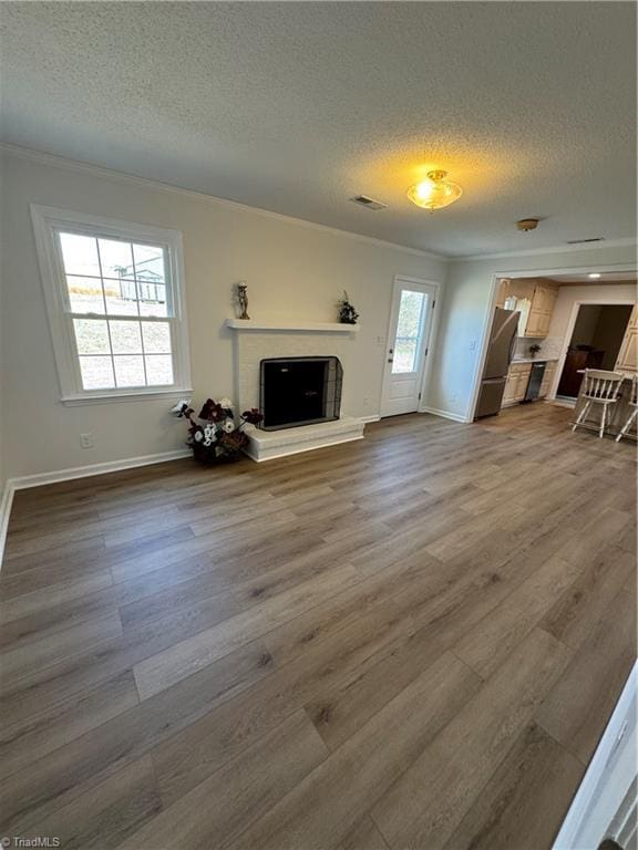 unfurnished living room with dark wood-type flooring, a fireplace with raised hearth, a textured ceiling, crown molding, and baseboards