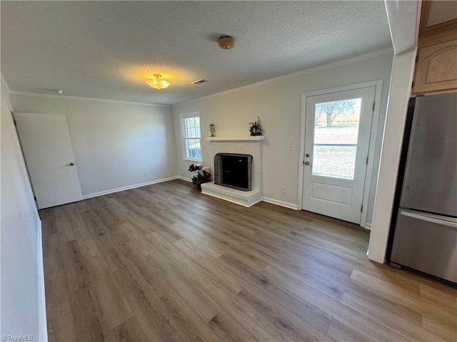 unfurnished living room with wood finished floors, a textured ceiling, a fireplace with raised hearth, and ornamental molding