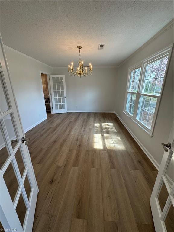 unfurnished dining area with french doors, dark wood-type flooring, a chandelier, and ornamental molding