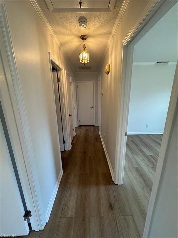 corridor with baseboards, an inviting chandelier, dark wood-type flooring, a textured ceiling, and crown molding