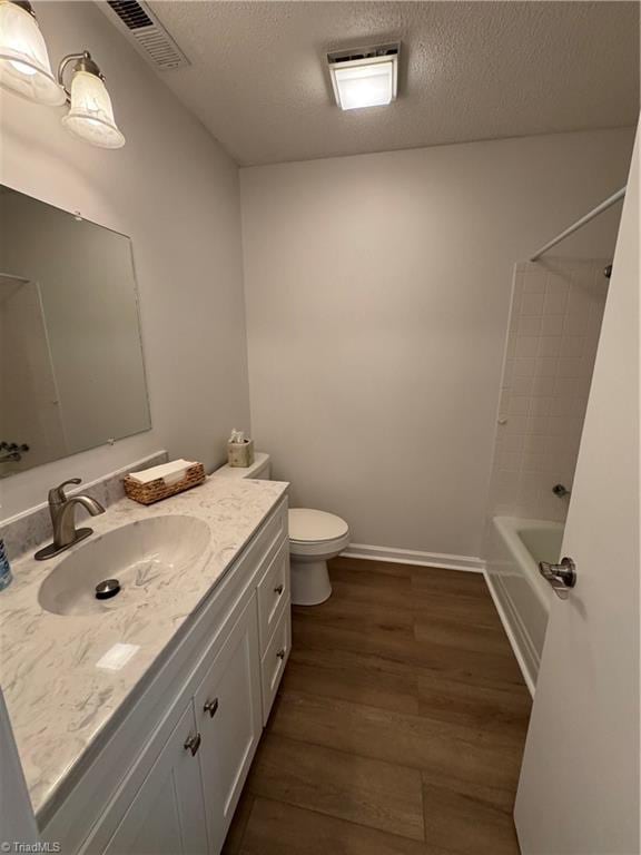 full bathroom featuring a textured ceiling, wood finished floors, vanity, and toilet