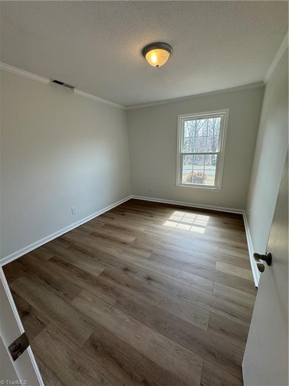 empty room with visible vents, a textured ceiling, crown molding, and dark wood-type flooring