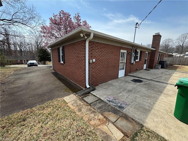 view of property exterior featuring central AC, brick siding, driveway, and a chimney