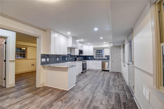 kitchen with white cabinetry, kitchen peninsula, hardwood / wood-style floors, decorative backsplash, and appliances with stainless steel finishes