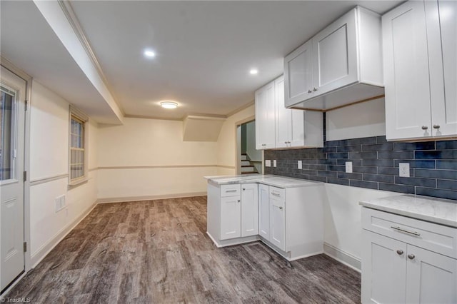 kitchen featuring white cabinetry, kitchen peninsula, crown molding, decorative backsplash, and hardwood / wood-style flooring