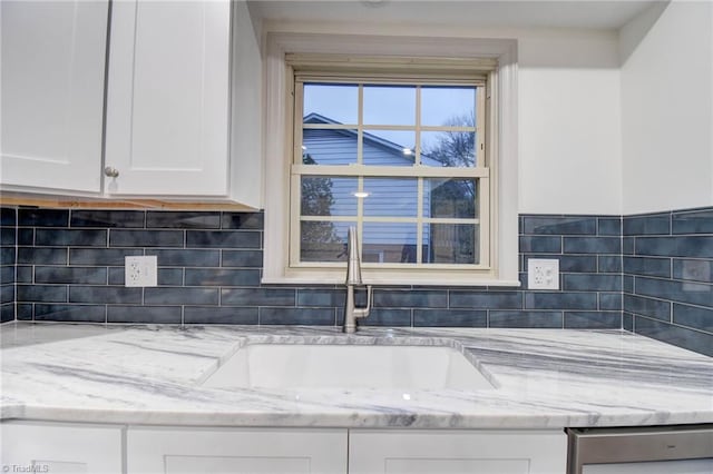 interior space with backsplash, sink, stainless steel dishwasher, light stone counters, and white cabinetry