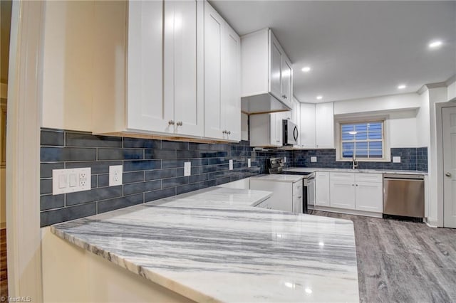 kitchen featuring light stone countertops, backsplash, stainless steel appliances, light hardwood / wood-style flooring, and white cabinetry